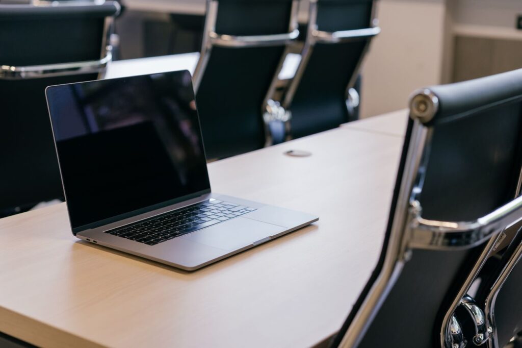 Open laptop on a wooden conference table with stylish black chairs in a modern office setting.